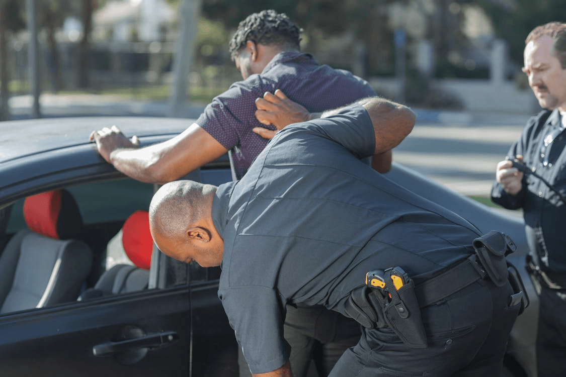 Person being detained by two police officers during a traffic stop illustrating the importance of staying calm to prioritize safety during a civil rights encounter