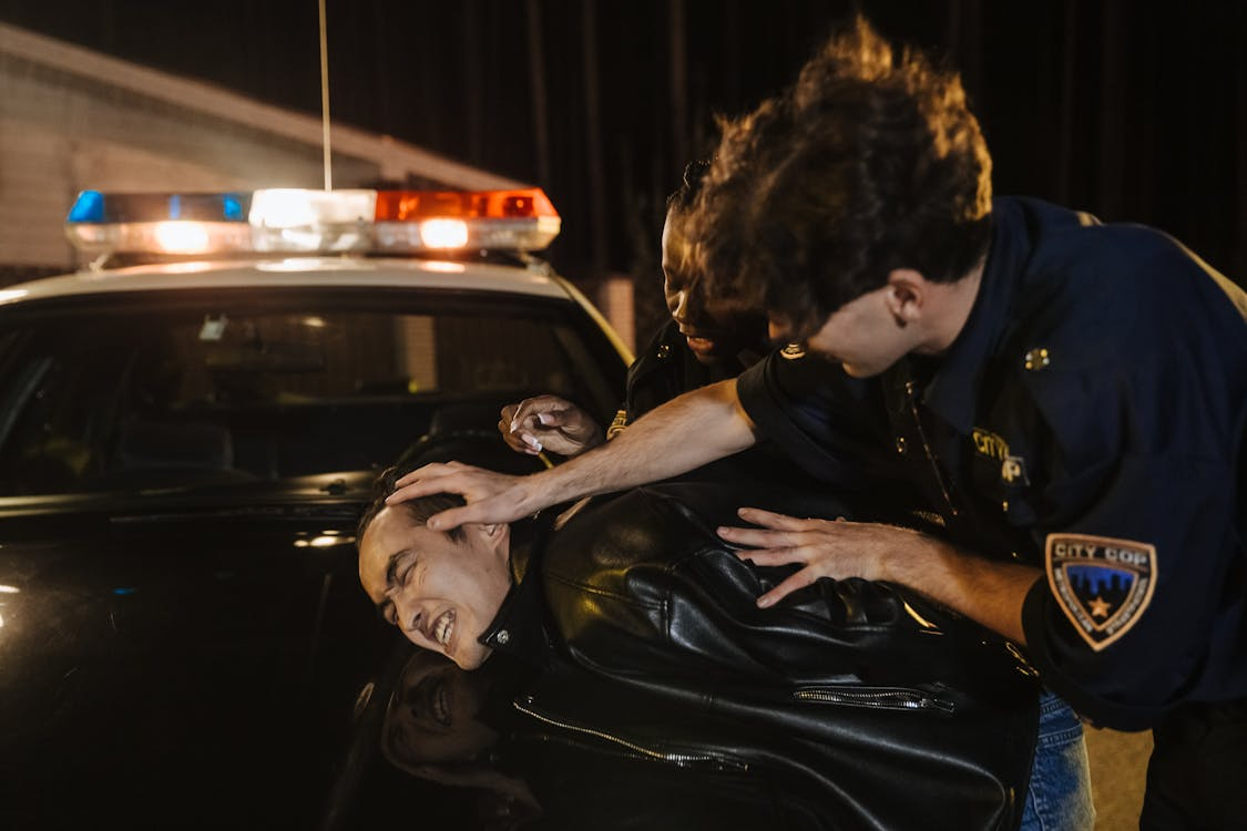 Person being forcibly restrained on police car hood by officers